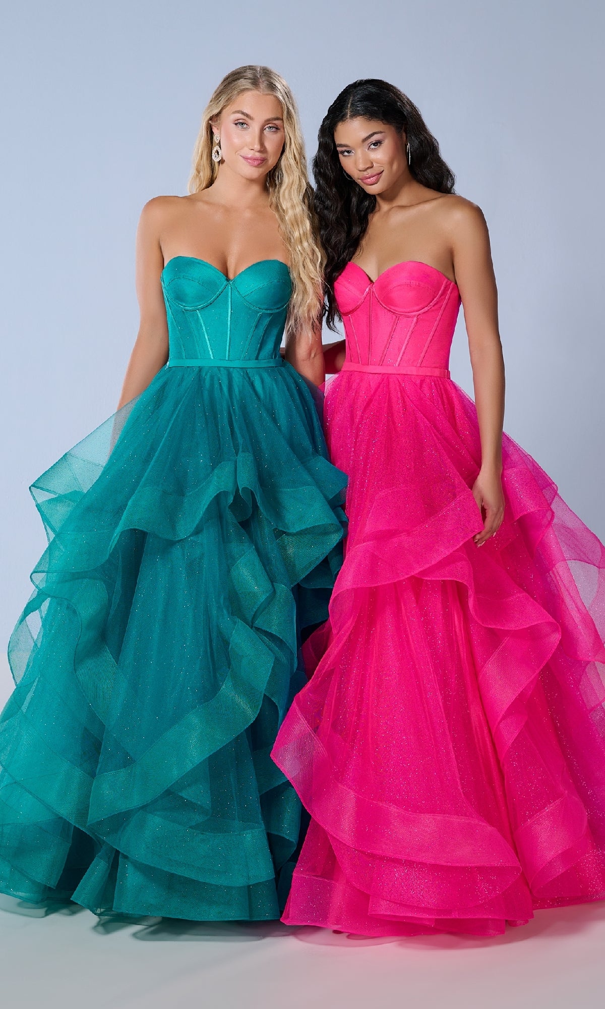 Two women stand side by side in Tiffany 16245 long prom dresses with strapless corset bodices and layered glitter tulle skirts—one dress is teal, the other bright pink.